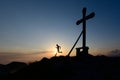 Silhouette of man running in the setting sun on top of a mountain with the cross