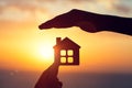 silhouette of man`s hand as a protecting roof over a small wooden house at Royalty Free Stock Photo