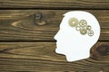 Silhouette of a man`s head with a brain made of iron gears on a wooden background.