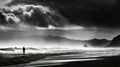 Silhouette of a man on a sandy beach in front of a mountain range with a dramatic sky, black and white, made with generative ai Royalty Free Stock Photo