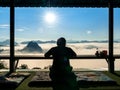 Silhouette of man sit at wooden terrace window looking at beautiful view of sea fog on mountains and morning sun at Ban Jabo, Mae