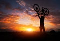 Silhouette the man stand in action lifting bicycle above his head on the meadow with sunset. Royalty Free Stock Photo