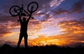 Silhouette the man stand in action lifting bicycle above his head on the meadow with sunset Royalty Free Stock Photo