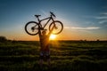 Man stand in action lifting bicycle above his head on the meadow with sunset Royalty Free Stock Photo