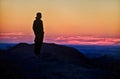 Silhouette of a man standing on top of a mountain and looking at the sunset