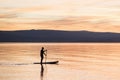 Silhouette of man at sunset standing on paddle board. Summer beach leisure activity.