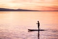 Silhouette of man at sunset standing on paddle board. Summer beach leisure activity.