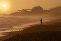 Silhouette of a man surf fishing at sunset with the San Onofre nuclear power plant in the background