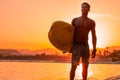 Silhouette man surfer in sunset light walking down beach with surfboard near waters edge enjoying summer time practice Royalty Free Stock Photo