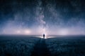 A silhouette of a man with a torch in a field, looking at lights on the horizon on a moody misty night. With a galaxy of stars ove Royalty Free Stock Photo