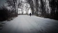 Silhouette of a man walking in the distance on a forest road in winter. There is a lot of snow. A lonely boy walks along a path in Royalty Free Stock Photo