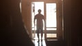 Silhouette of a man walking towards the exit along the corridor to sunlight during sunset time