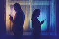 Silhouette of a man and a woman with phones at the night window. Couple husband and wife having relationship problems in the Royalty Free Stock Photo
