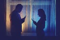 Silhouette of a man and a woman with phones at the night window. Couple husband and wife having relationship problems in the Royalty Free Stock Photo