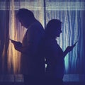 Silhouette of a man and a woman with phones at the night window. Couple husband and wife having relationship problems in the Royalty Free Stock Photo