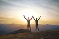 Silhouette of man and woman standing on edge of mountain and holding hands up on sunset sky and mountains background. Royalty Free Stock Photo