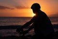 Silhouette of mature man cycling his bicycle at the beach with a magnificent orange sunset. Sunbeam at the horizon