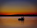 Silhouette of men fishing in a boat on calm lake after sunset