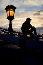 The silhouette of the man sitting on the Chain Bridge in Budapest, Hungary near the lightning street lamp.