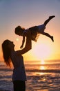 Silhouette of mom and daughter on the beach. Happy Woman throws up a child. A mother plays with her child at dusk and Royalty Free Stock Photo