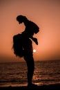 Silhouette of a mother carrying and playing with her little daughter by the sea at sunset Royalty Free Stock Photo