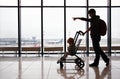 Silhouette of mother with her toddler son in stroller against the window at the airport. Mom points the direction with her finger