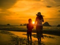 Silhouette of mother holding kid hand and walk on the beach during sunset. Royalty Free Stock Photo