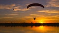 Silhouette of moto paragliders flying at summer sunset. Two powered paragliders over the lake