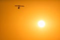 Silhouette of a motor glider flying high in orange sunset sky on sun disc background Royalty Free Stock Photo