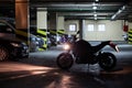 Silhouette of motorcycle standing with running engine in front of parked vehicles in underground parking area
