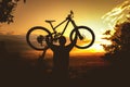 Silhouette of a mountain biker holding a bicycle over his head at sunset. MTB, enduro, freeride background. Royalty Free Stock Photo