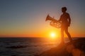 Silhouette of musician with trumpet on rocky sea coast during sunset. Royalty Free Stock Photo
