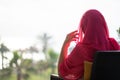 Silhouette of muslim, arab woman in red head scarf, hijab sitting on the armchair on terrace and looking on sunset palm sea beach. Royalty Free Stock Photo