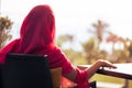 Silhouette of muslim, arab woman in red head scarf, hijab sitting at the table on terrace and looking sunset palm sea beach Royalty Free Stock Photo