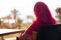 Silhouette of muslim, arab woman in red head scarf, hijab sitting at the table on terrace and looking sunset palm sea beach Royalty Free Stock Photo