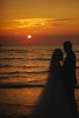 Silhouette of newlyweds bride and groom are hugging on sunset or sunrise on beach. Loving couple by the sea. Ocean Royalty Free Stock Photo