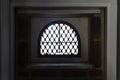 Silhouette of and old arched, small window seen from inside. Close up of the window with bars against stone wall Royalty Free Stock Photo