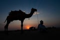 Silhouette of old cameleer and his camel at sand dunes of Thar desert, Rajasthan, India. Cloud with setting sun, sky in the Royalty Free Stock Photo