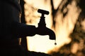 Silhouette of old vintage metal tap leaking water droplet in dry summer morning / evening , water shortage , crisis , scarcity