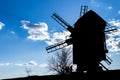 Silhouette of an old wooden mill against the background of a clear blue sky with a couple of clouds, several contours of people Royalty Free Stock Photo