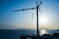 Silhouette, outline of the crane on the construction site against the blue sky and the sea. Details of the building, ribbed walls