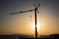 Silhouette, outline of the crane on the construction site against the setting sun and the sea. Details of the building, ribbed