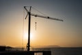 Outline, silhouette of the crane on the construction site against the setting sun and the sea. Details of the building