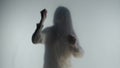 Silhouette of panicked woman in fog behind frosted glass or curtain. The woman is pounding on the glass with her fists