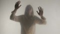 Silhouette of panicked woman in fog behind frosted glass or curtain. The woman is tapping her palms on the glass, hoping