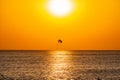 Silhouette of a parachute and a skydiver against the background of a bright burning sunset over the sea