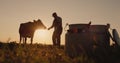 The silhouette of a pastoralist stands near his cow. Milk cans are in the foreground.