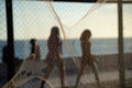 Silhouette of pedestrians, through a net, walking along the edge of a beach against the sunset