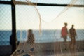 Silhouette of pedestrians, through a net, walking along the edge of a beach against the sunset