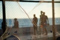 Silhouette of pedestrians, through a net, walking along the edge of a beach against the sunset